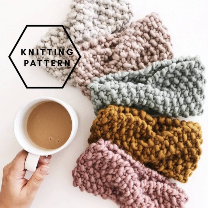Four chunky, hand-knitted headbands in pink, mustard yellow, green, and beige next to a mug of coffee.